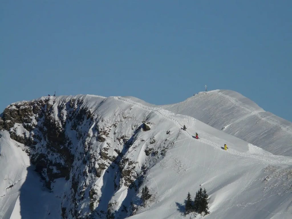 Skiers on a narrow cat track amidst majestic mountain scenery, capturing the essence of cat track skiing.